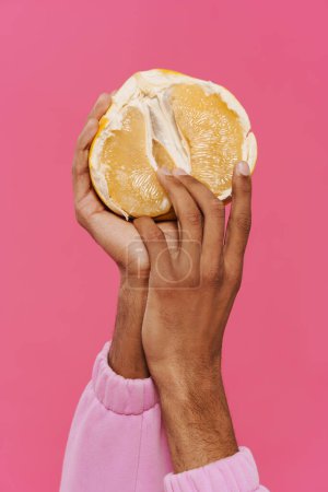 Foto de Black man's hands holding and showing pamelo at camera isolated over pink background - Imagen libre de derechos