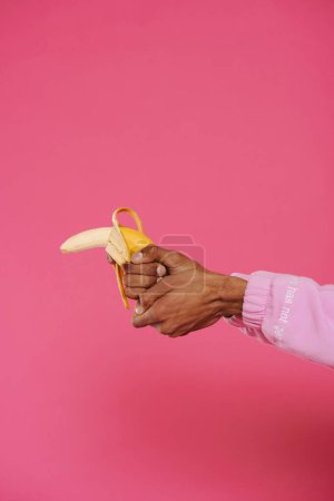 Photo for Black man's hand holding and showing gun gesture with banana isolated over pink background - Royalty Free Image