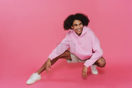 Photo for Young caribbean man with piercing smiling and squatting isolated over pink background - Royalty Free Image