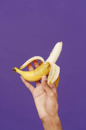 Foto de Black man's hand holding and showing banana at camera isolated over purple background - Imagen libre de derechos