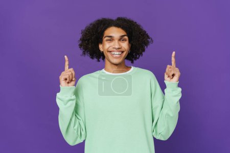 Photo for Young caribbean man smiling and pointing fingers upward isolated over purple background - Royalty Free Image