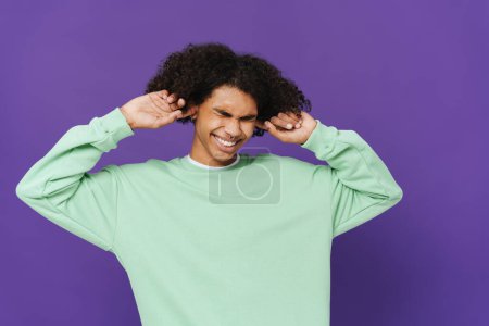 Photo for Young caribbean man with piercing plugging his ears isolated over purple background - Royalty Free Image