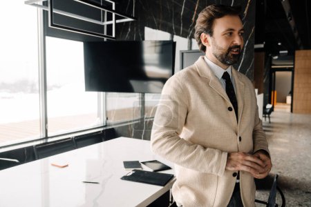 Photo for Portrait of successful confident bearded european businessman in jacket looking aside with table on the background - Royalty Free Image