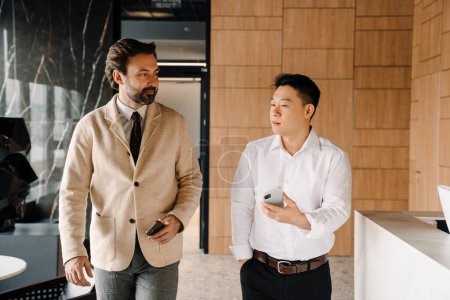 Photo for Two succesful elegant business people talk and walk holding their phones in modern office building - Royalty Free Image