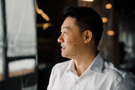 Foto de Close up portrait of middle aged cheerful confident asian business person in white shirt looking aside indoor - Imagen libre de derechos