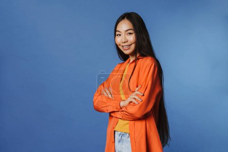 Téléchargez les photos : Young asian woman wearing shirt smiling while looking at camera isolated over blue background - en image libre de droit