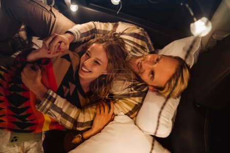 Téléchargez les photos : Heureux jeune couple blanc souriant et couché ensemble en voiture à l'extérieur - en image libre de droit