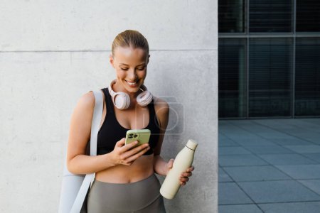 Téléchargez les photos : White young woman using mobile phone after yoga practice outdoors - en image libre de droit