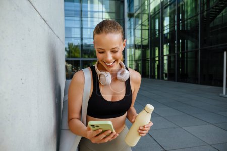 Foto de Mujer joven blanca usando teléfono móvil después de practicar yoga al aire libre - Imagen libre de derechos