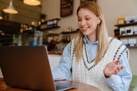Téléchargez les photos : Blonde femme blanche écouter de la musique tout en travaillant avec ordinateur portable au café à l'intérieur - en image libre de droit