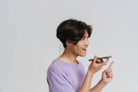 Foto de Joven asiático hombre usando camiseta gesto y hablando en el teléfono celular aislado sobre fondo blanco - Imagen libre de derechos