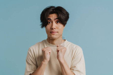 Photo for Shocked asian man wearing t-shirt gesturing and looking at camera isolated over blue background - Royalty Free Image
