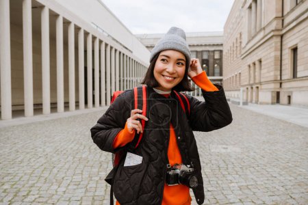 Téléchargez les photos : Young joyful asian woman tourist in warm clothes walking through the old town street - en image libre de droit
