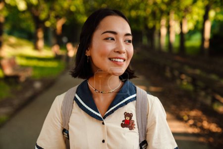 Téléchargez les photos : Young beautiful smiling asian woman with backpack walking outdoors in green park - en image libre de droit