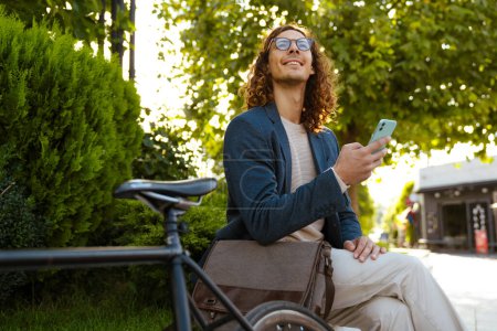 Photo for Ginger european man using mobile phone while sitting with bicycle in city park - Royalty Free Image