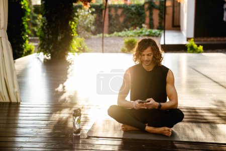 Téléchargez les photos : Young ginger man using mobile phone during yoga practice outdoors - en image libre de droit