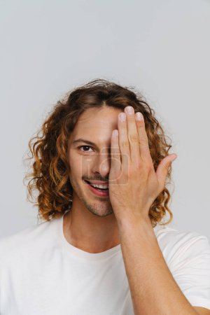 Téléchargez les photos : Ginger european man with curly hair smiling and covering his eye isolated over white background - en image libre de droit