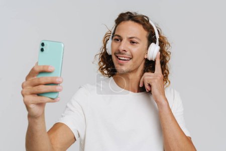 Téléchargez les photos : Ginger european man in headphones smiling and using cellphone isolated over white background - en image libre de droit
