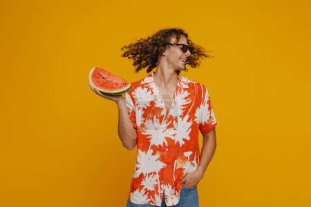 Téléchargez les photos : Ginger man in sunglasses laughing while dancing with watermelon isolated over yellow background - en image libre de droit