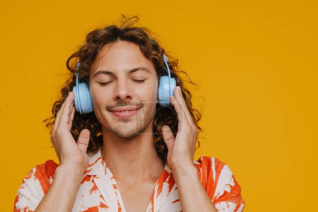 Téléchargez les photos : Ginger homme européen dans les écouteurs souriant et écouter de la musique isolée sur fond jaune - en image libre de droit