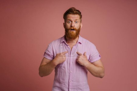 Photo for Ginger white man expressing surprise and pointing fingers at himself isolated over pink background - Royalty Free Image