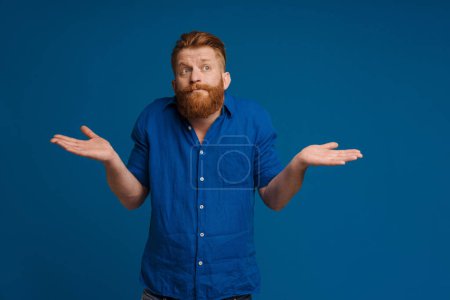 Photo for Ginger white man with beard looking at camera and holding copyspace isolated over blue background - Royalty Free Image