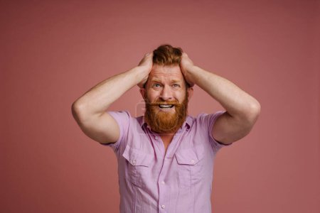 Photo for Ginger scared man holding his head and screaming at camera isolated over pink background - Royalty Free Image