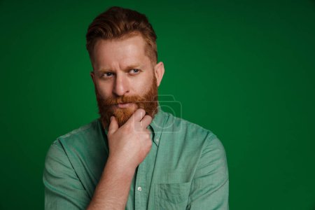 Photo for Ginger white man with beard looking aside and holding his chin isolated green pink background - Royalty Free Image