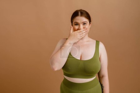 Photo for White young woman with ginger hair posing while covering her mouth isolated over beige background - Royalty Free Image