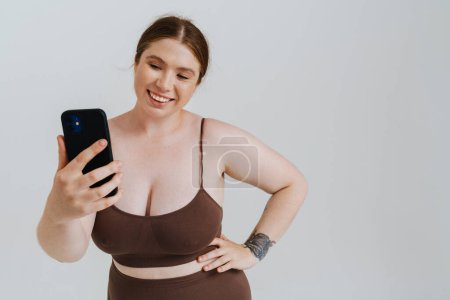 Photo for European woman smiling while taking selfie photo on cellphone isolated over white background - Royalty Free Image