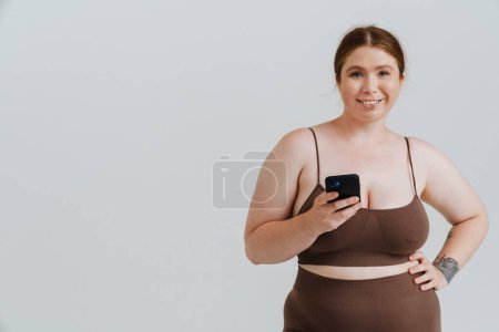 European woman with ginger hair smiling while using mobile phone isolated over white background