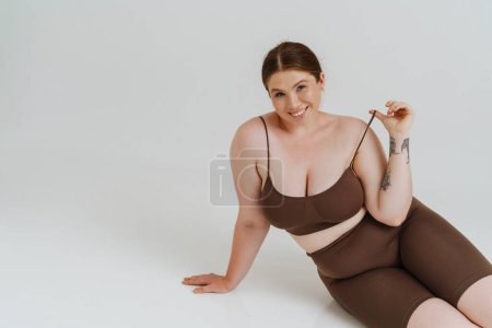 Téléchargez les photos : Femme européenne aux cheveux roux souriant assis sur le sol isolé sur fond blanc - en image libre de droit