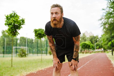 Photo for Ginger bearded sportsman resting while working out in park outdoors - Royalty Free Image