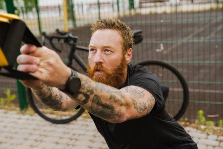 Photo for Ginger bearded sportsman doing exercise while working out on playground outdoors - Royalty Free Image