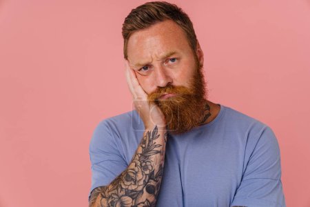 Photo for Ginger perplexed man with beard frowning and looking at camera isolated over pink background - Royalty Free Image