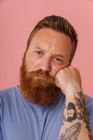 Photo for Ginger perplexed man with beard frowning and looking at camera isolated over pink background - Royalty Free Image
