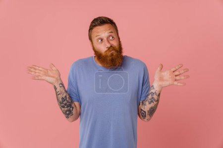 Photo for Ginger perplexed man with beard gesturing and looking aside isolated over pink background - Royalty Free Image