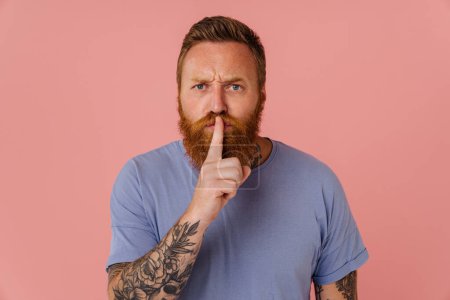 Photo for Ginger white man with tattoo frowning and showing silence gesture isolated over pink background - Royalty Free Image
