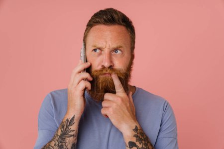Photo for Ginger white man talking on cellphone and frowning isolated over pink background - Royalty Free Image