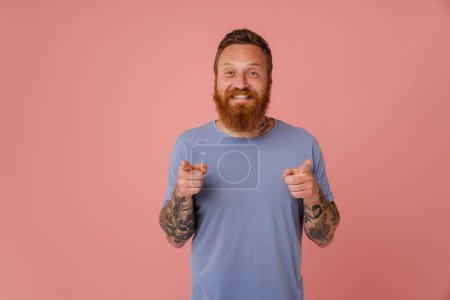Téléchargez les photos : Gingembre blanc homme souriant et pointant les doigts à la caméra isolé sur fond rose - en image libre de droit