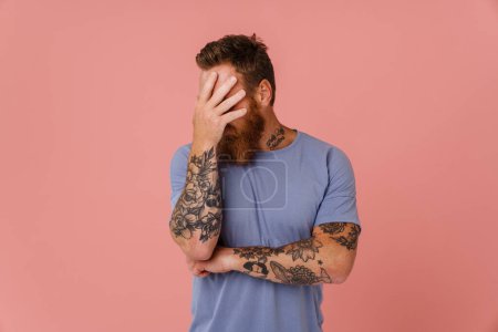 Photo for Ginger white man with tattoo posing and covering his face isolated over pink background - Royalty Free Image