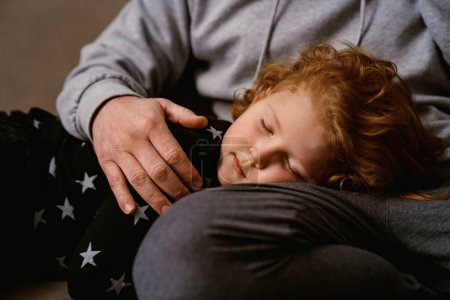 Foto de Lindo poco jengibre chico durmiendo en padre rodillas en casa - Imagen libre de derechos