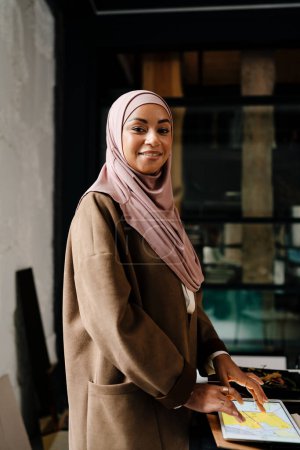 Téléchargez les photos : Femme musulmane designer portant hijab travaillant sur tablette à l'atelier - en image libre de droit