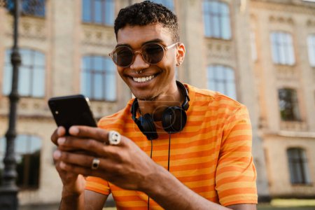 Téléchargez les photos : Jeune homme brune noire portant des lunettes de soleil en utilisant un téléphone portable à l'extérieur - en image libre de droit