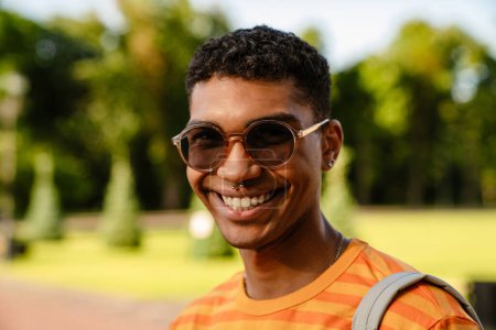 Foto de Joven morena negra hombre con piercing y gafas de sol caminando en el parque - Imagen libre de derechos