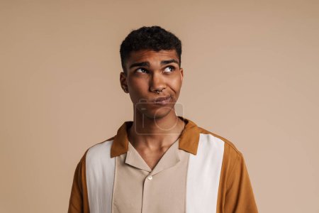 Photo for Perplexed black man grimacing while looking aside isolated over beige background - Royalty Free Image