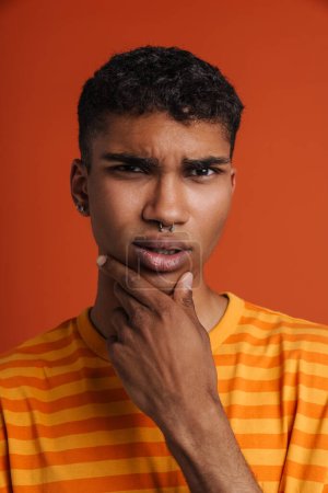 Photo for Young black man with piercing frowning and holding his chin isolated over red background - Royalty Free Image