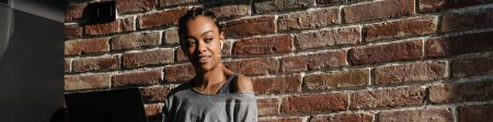 Téléchargez les photos : Souriant afro-américaine fille dans les écouteurs de travail avec ordinateur portable à la maison - en image libre de droit