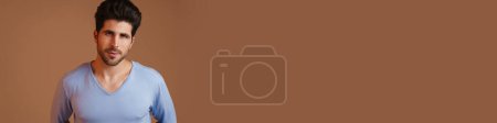 Téléchargez les photos : Agréable beau jeune homme posant et regardant la caméra isolé sur fond beige - en image libre de droit