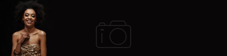 Téléchargez les photos : Heureuse femme afro-américaine en robe de soirée riant de la caméra isolée sur fond noir - en image libre de droit